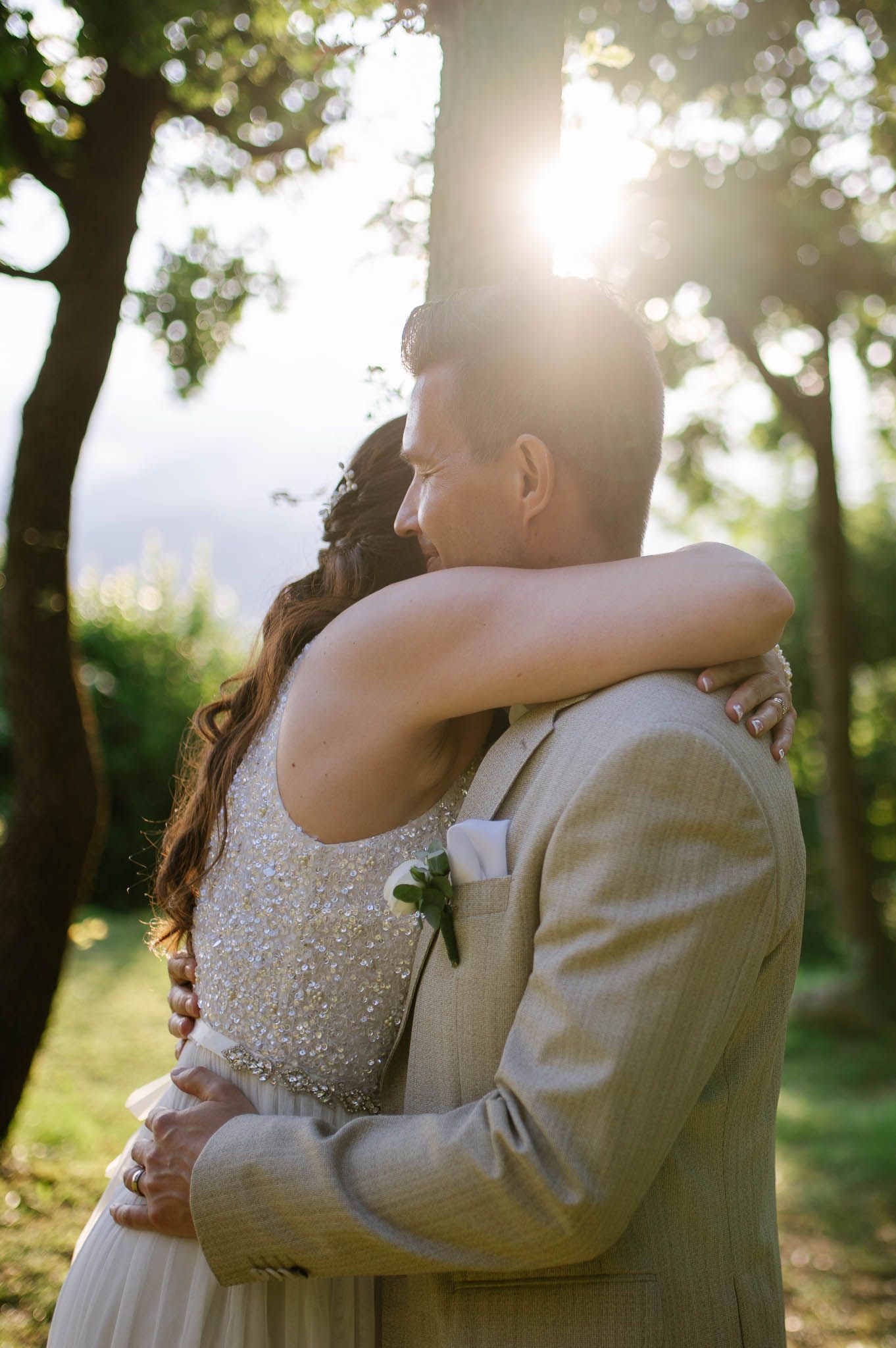 Newlyweds share a romantic embrace in golden sunlight filtering through lush garden trees.