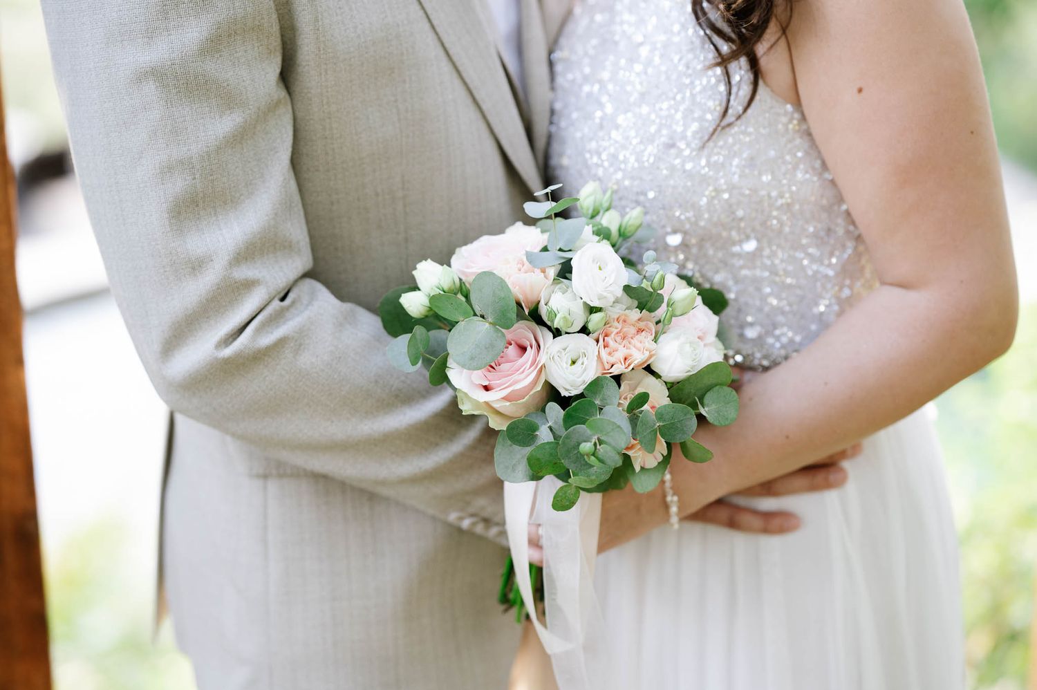 Bride and groom holding a small blush and white rose bouquet with eucalyptus, bride wearing a beaded gown.
