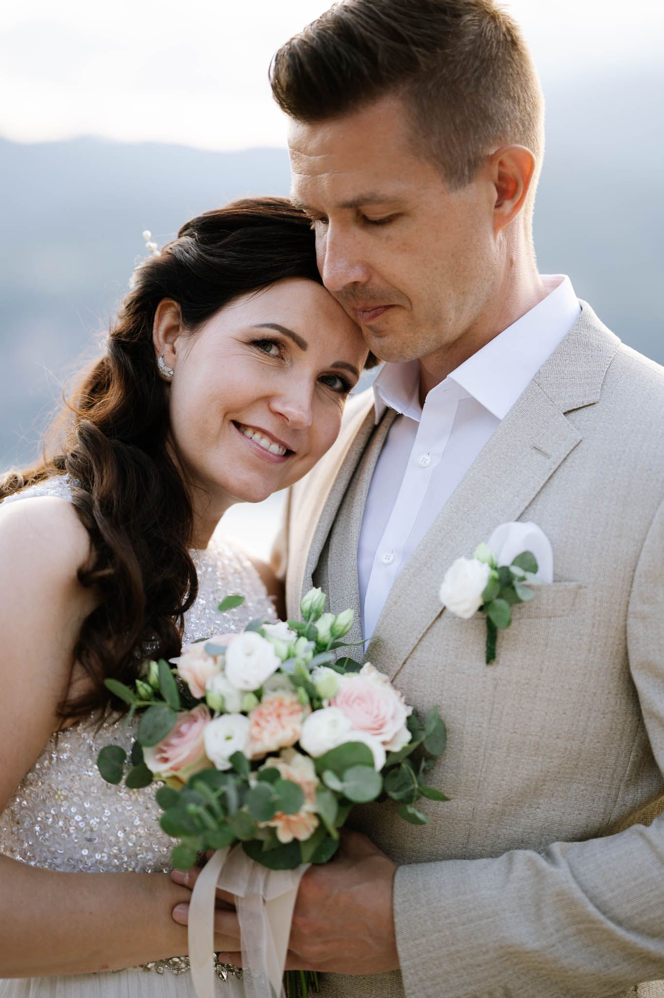 Happy bride and groom embracing outdoors, holding a bouquet of pink and white roses at their wedding.