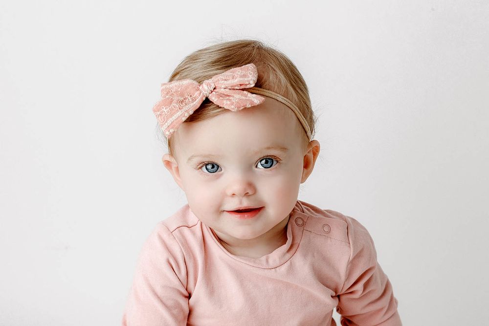 Sweet baby girl with blue eyes wearing pink outfit and matching bow headband.