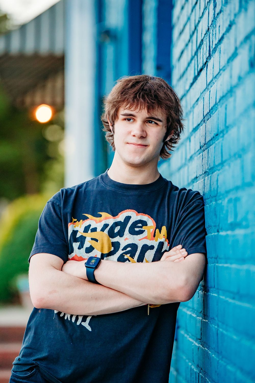 Young man in Hyde Park t-shirt leaning against blue brick wall outdoors.