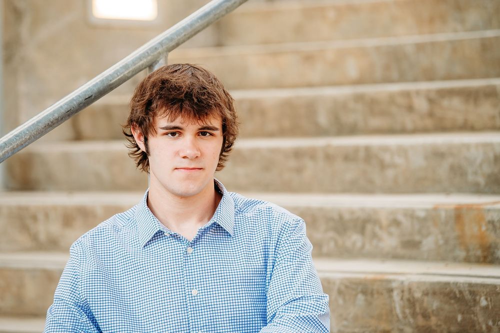 Young man in blue button-up shirt sitting on stone steps outdoors.