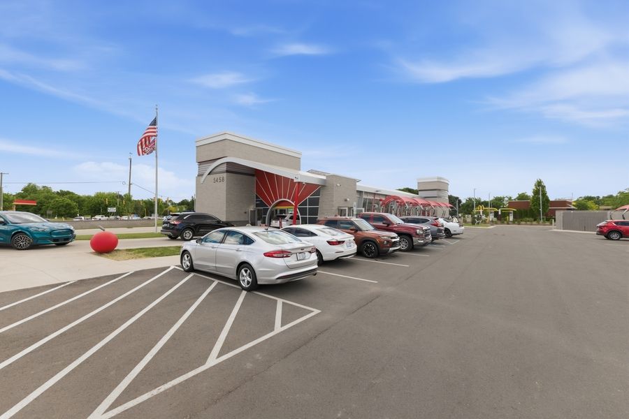 Busy commercial parking lot with multiple cars parked outside a retail building featuring a red sunburst sign on a sunny day.