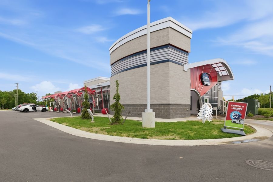 Modern commercial building with red accents and curved architecture, surrounded by a parking lot and landscaped greenery.
