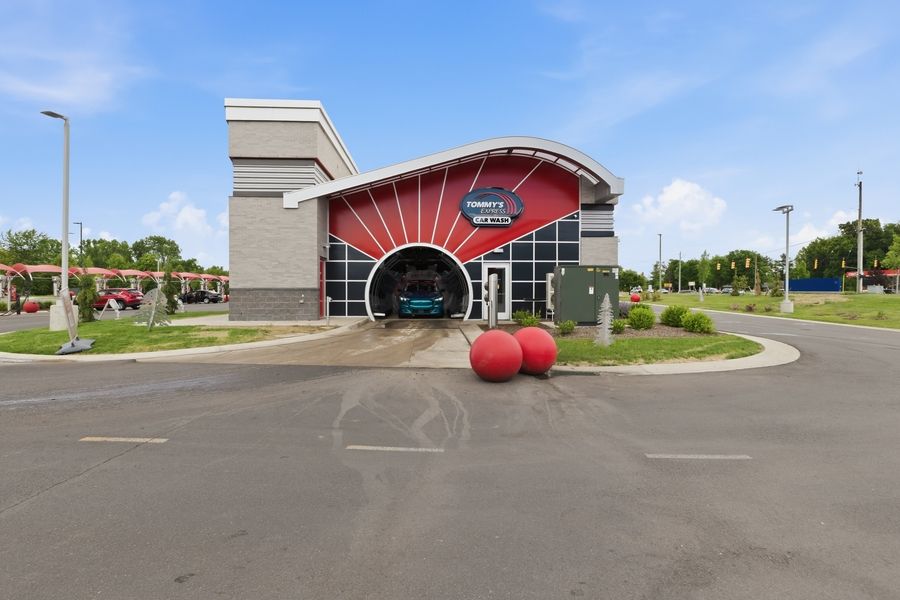 Modern car wash facility with a vibrant red sunburst facade, large decorative red spheres, and a vehicle entering the tunnel.