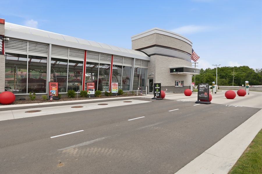 Exterior view of a modern Tommy's Car Wash facility with red accents and large windows along a paved road.