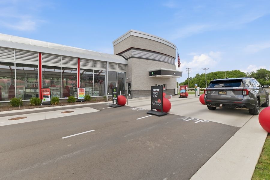 Exterior view of a modern Tommy's Express car wash with red accents, drive-through lanes, and decorative red spheres out front.