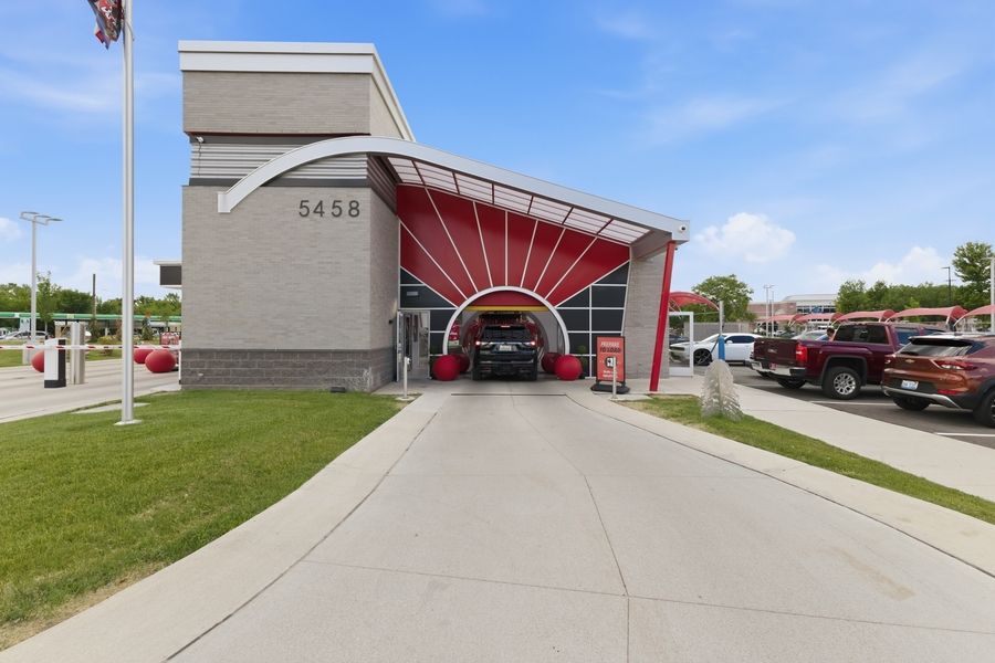 Modern red and white car wash facility at 5458 with covered drive-through entrance and parking lot on a sunny day.