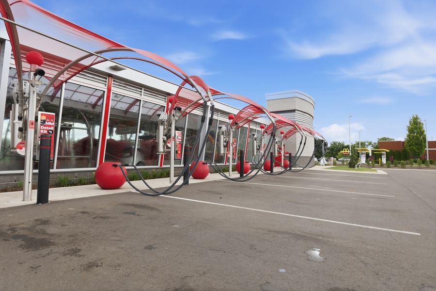 Modern commercial building entrance with distinctive red circular metal arch sculptures and covered walkway under blue sky.