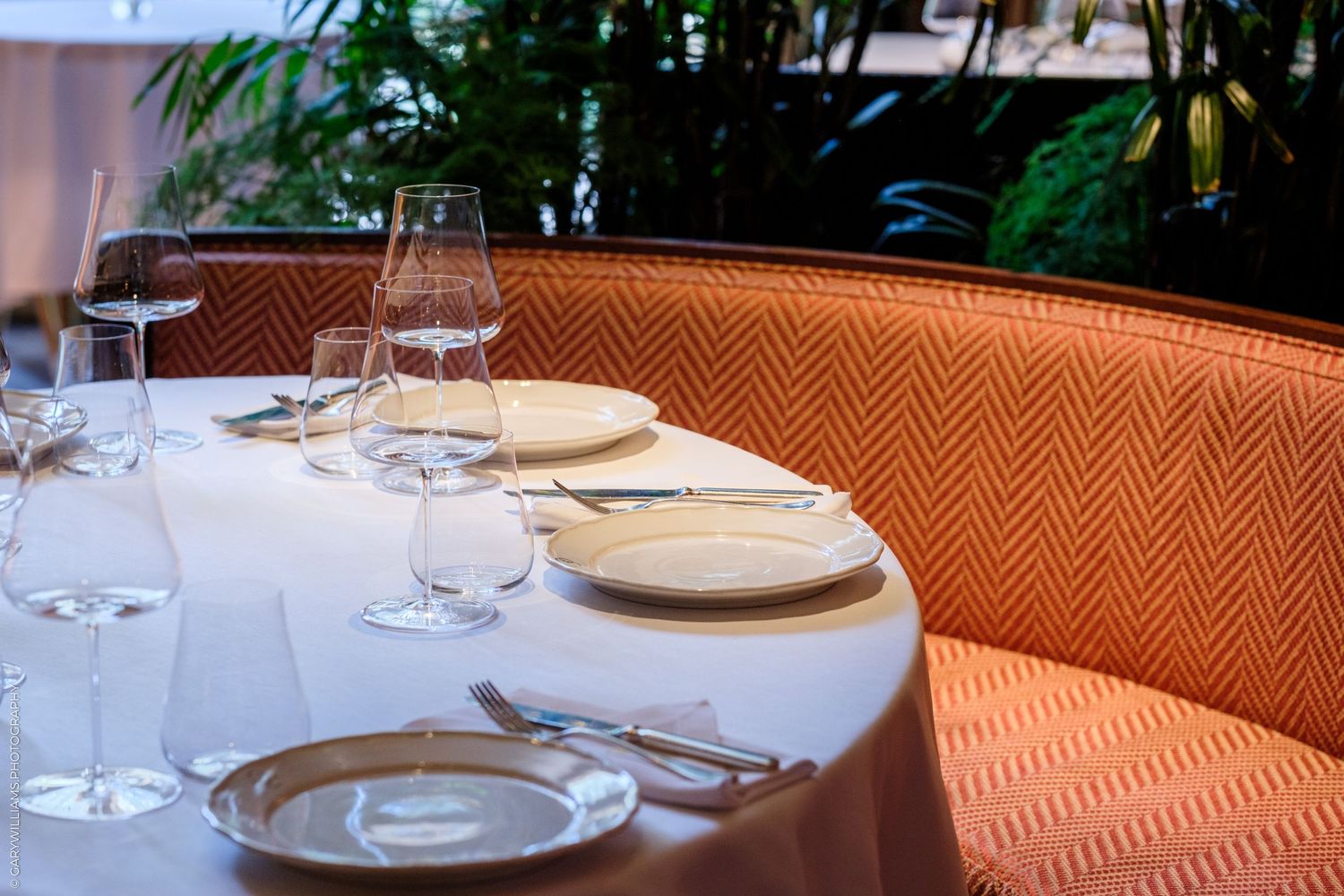 Elegant restaurant booth with orange herringbone upholstery, white tablecloth, crystal wine glasses, and white plates set for dining.