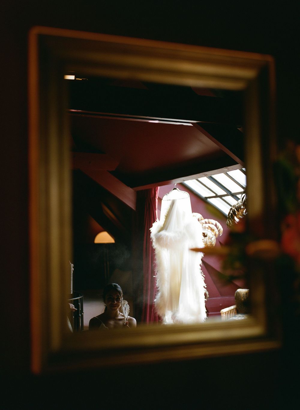 A bride in a white gown reflected in a gold-framed mirror inside a dark, elegant room with red walls. hotel particulier montmartre wedding,