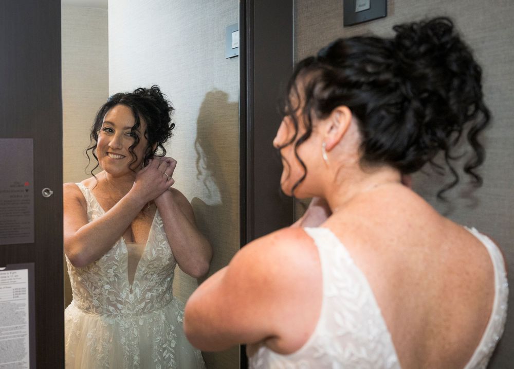 Bride smiling at her reflection in a mirror while adjusting her wedding dress before the ceremony.