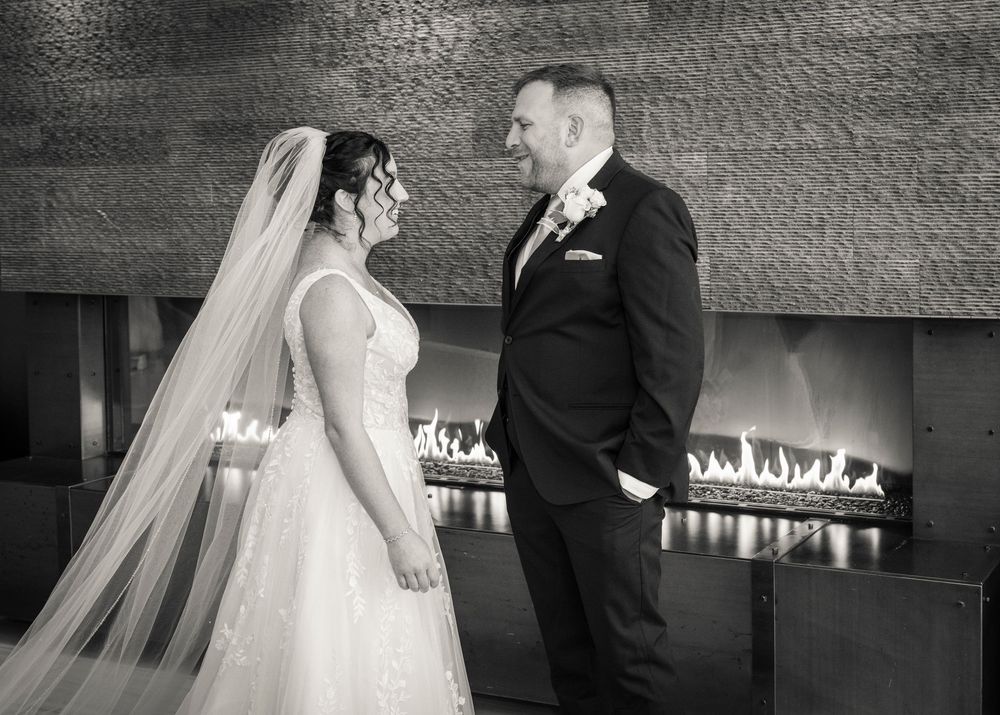 Black and white photo of a bride and groom sharing a joyful moment before a fireplace on their wedding day.