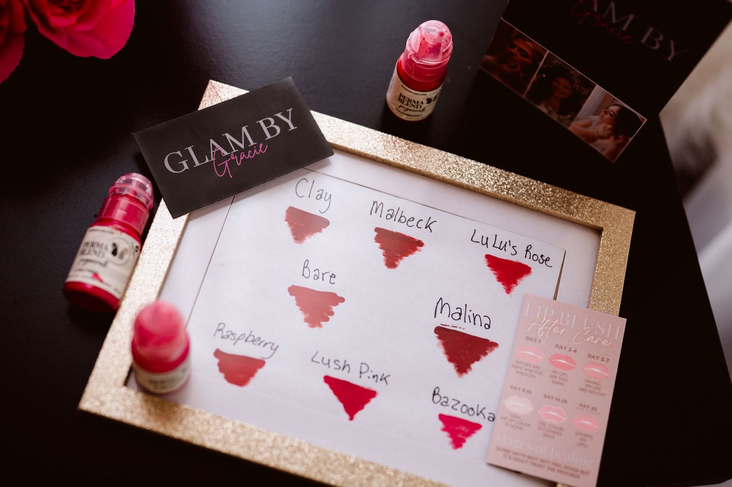 Glam By lipstick swatches on white paper showing shades like Clare, Malbeck, Lulas Rose, Haze, Malina, Raspberry, Crush Pink, and Bazzania.