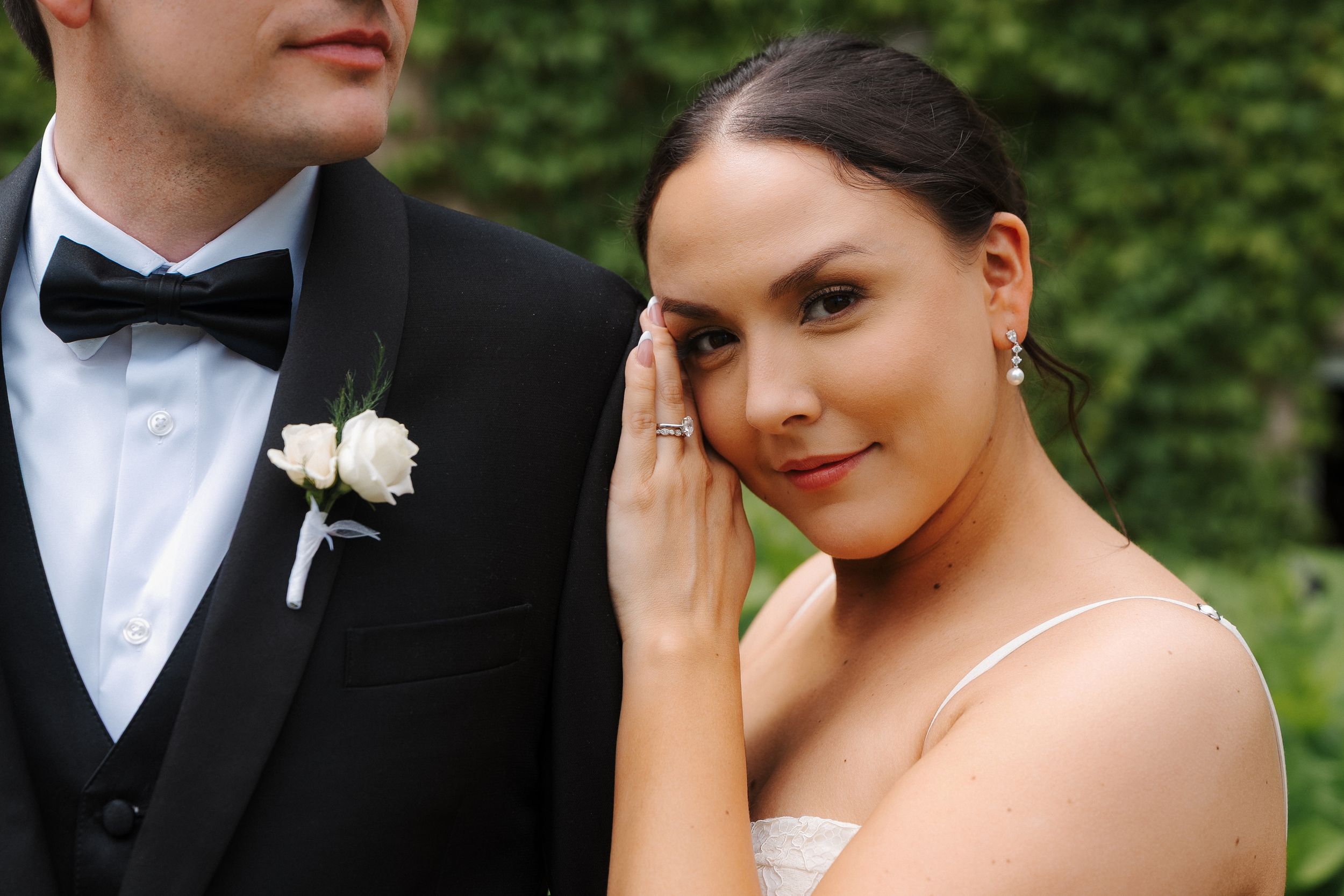 Bride wiping a tear on her wedding day, wearing a white dress and earrings, standing beside groom in black tuxedo.