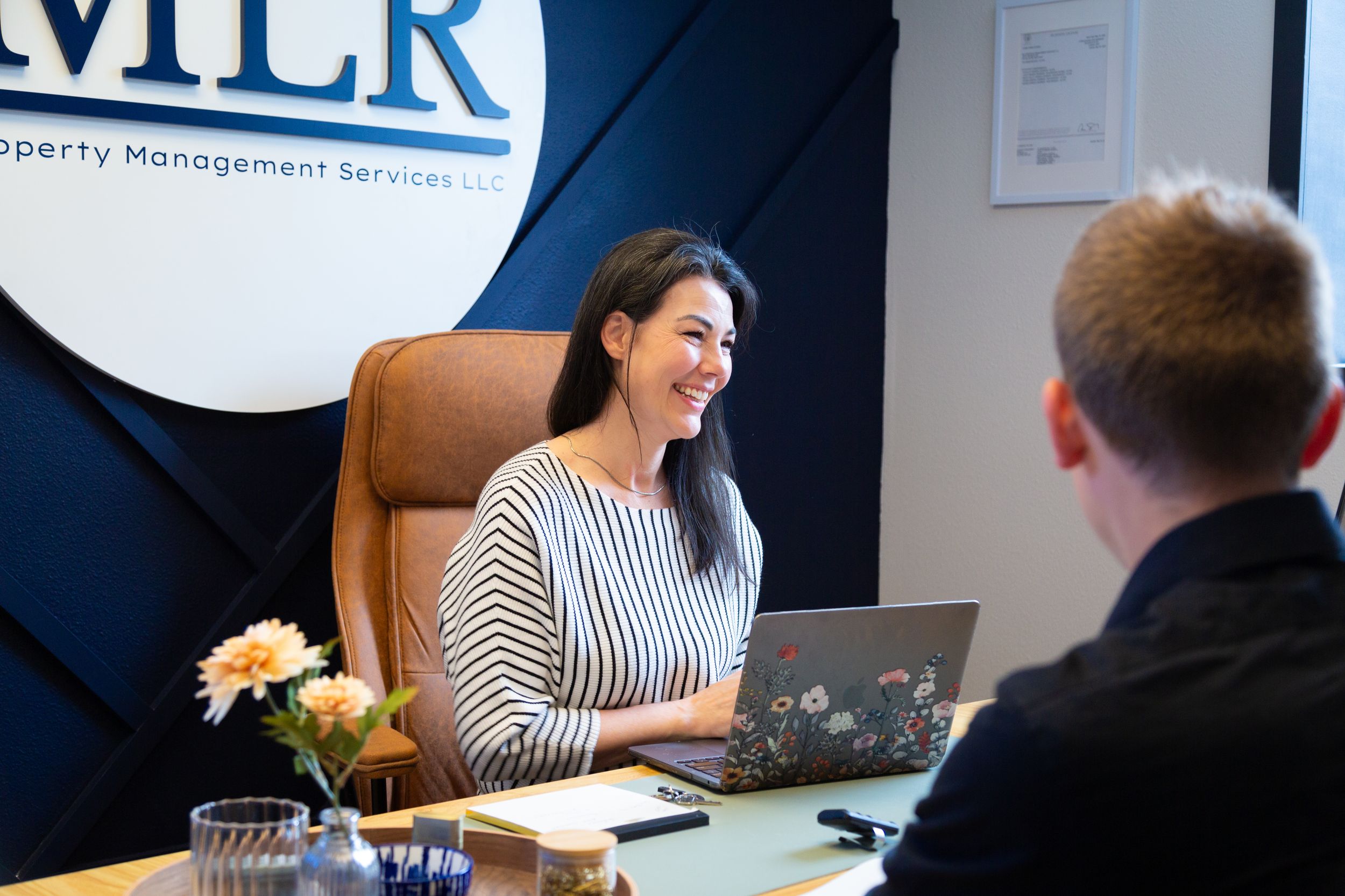 A smiling woman works on a laptop at MLR Property Management Services LLC office desk.