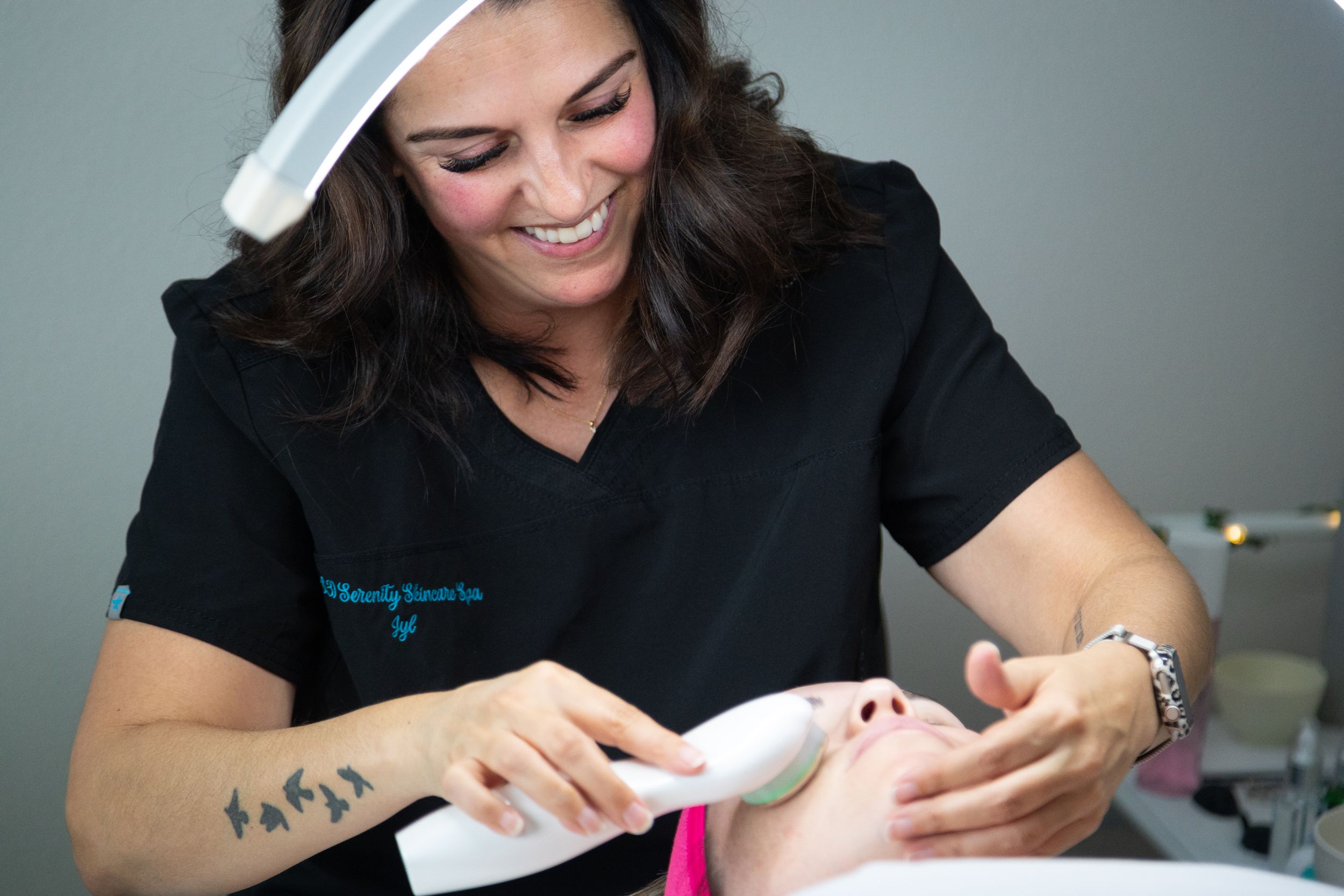 Smiling esthetician applying skincare treatment to client's face in a professional beauty salon setting.