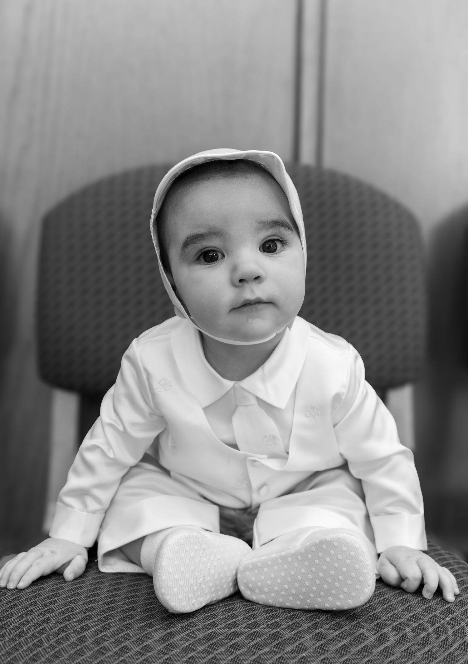 Series of black and white portraits showing baby in white outfit lying on cushioned surface looking at camera.