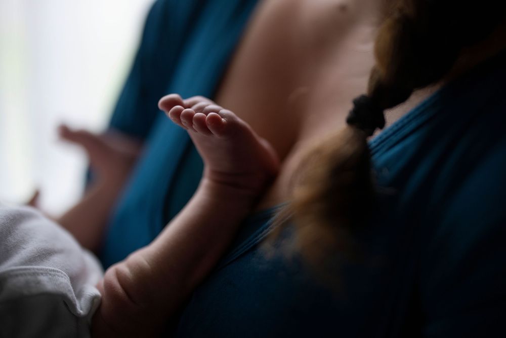Close-up of a newborn baby's tiny hand resting on a mother's chest during breastfeeding.