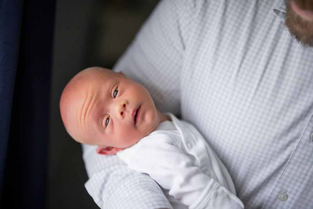 A newborn baby with wide eyes is cradled in a parent's arms in a tender close-up photo.