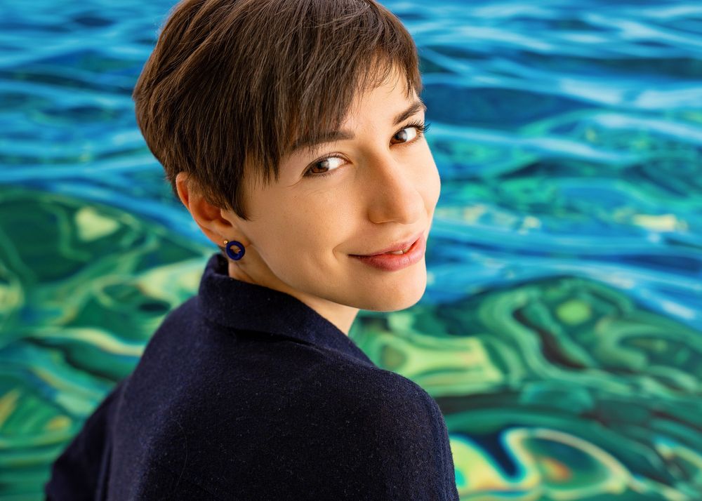 Artist shown against vibrant blue and green water-inspired artwork background in studio setting.