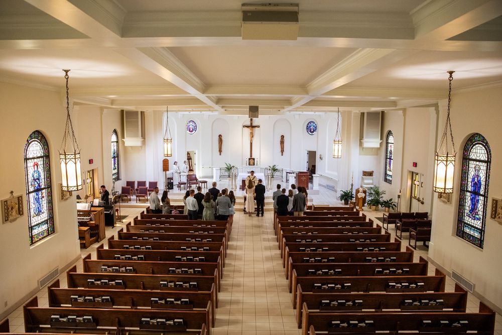 Aerial view of a traditional Catholic church interior with wooden pews, stained glass windows, and altar during a ceremony.