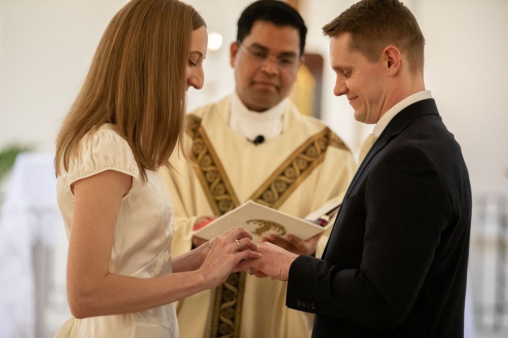 Couple exchanging wedding rings at altar with officiant in gold vestments during church ceremony.