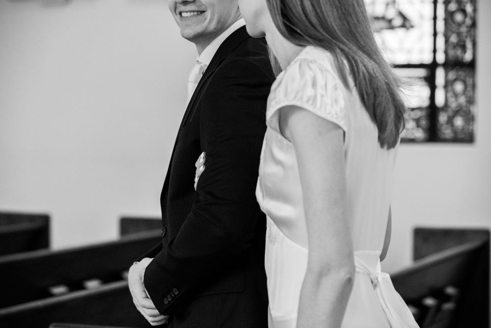 Black and white photo of a smiling couple in wedding attire standing in a church aisle.
