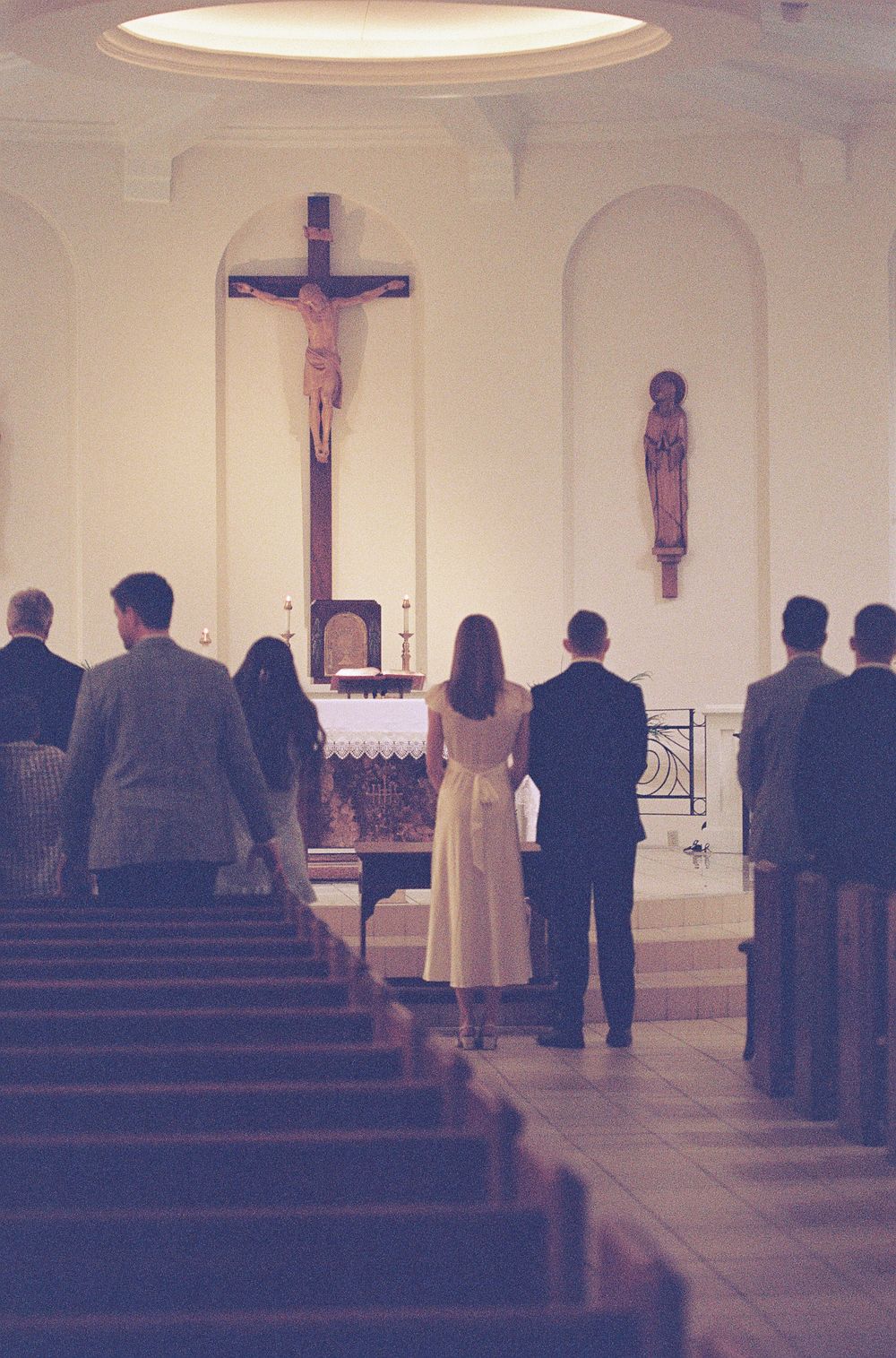 Wedding ceremony in a Catholic church with bride and groom standing before a crucifix at the altar.