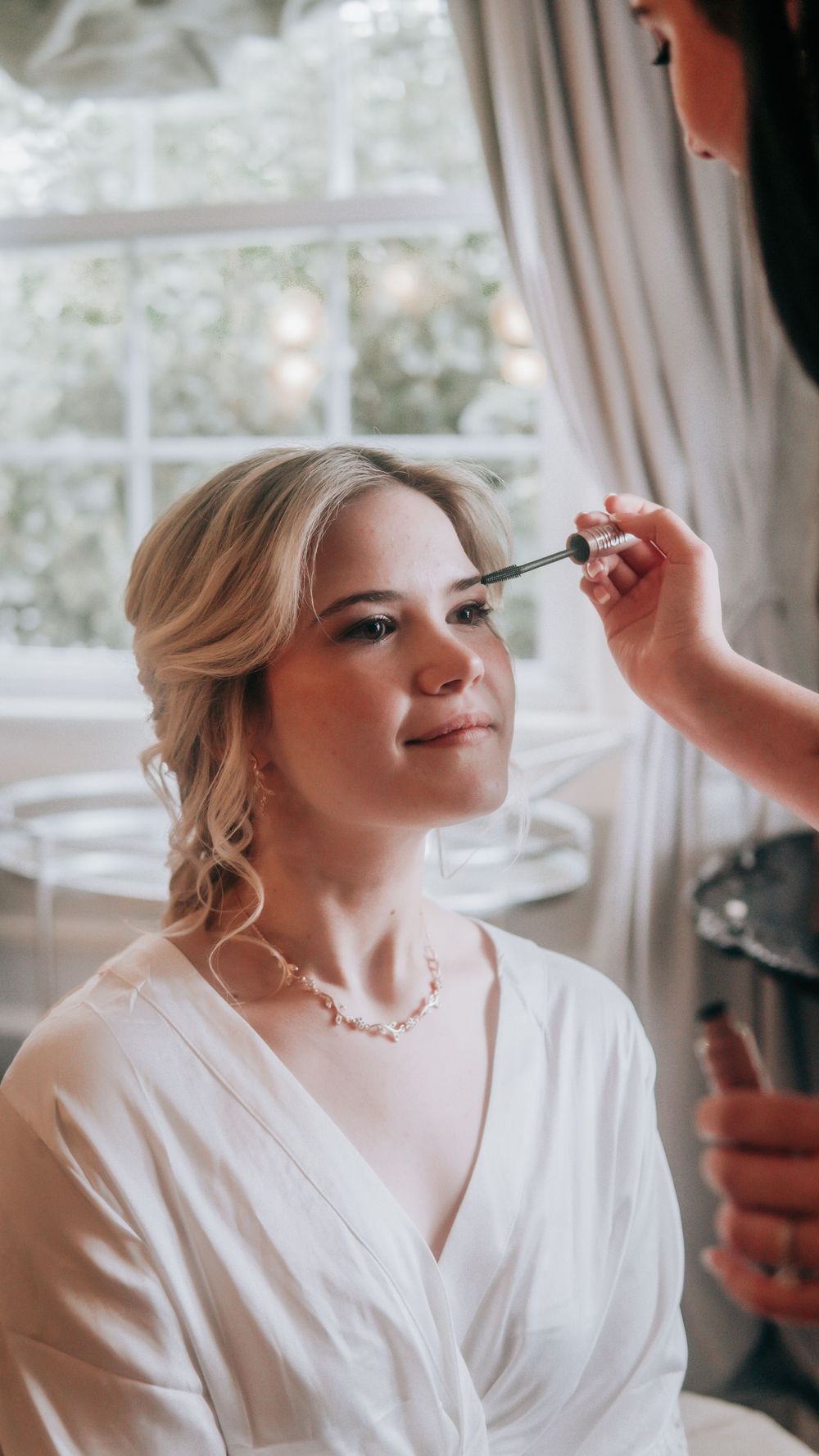 Bride getting makeup applied by artist before wedding ceremony.