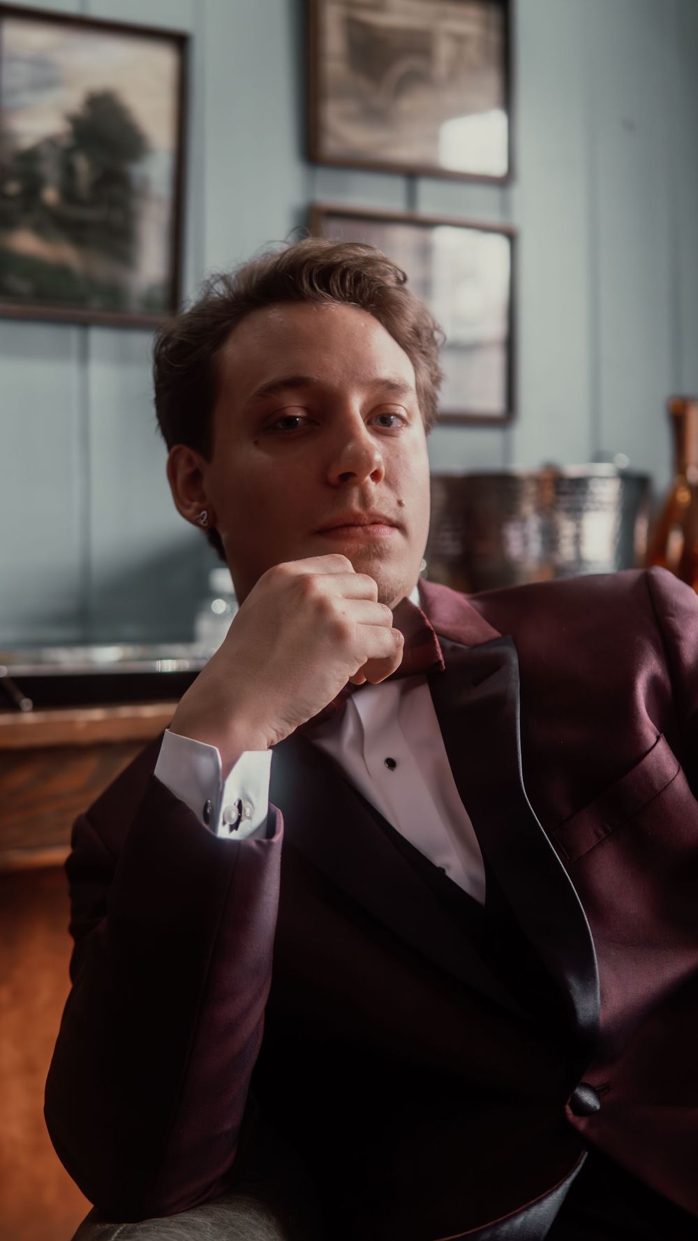 Groom in burgundy tuxedo sitting pensively before wedding.