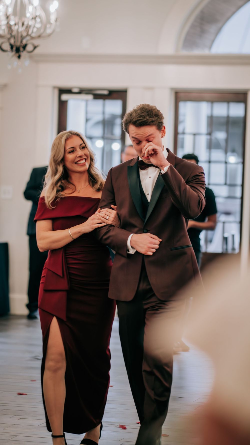 Groom in burgundy tux dancing emotionally with woman in red dress.