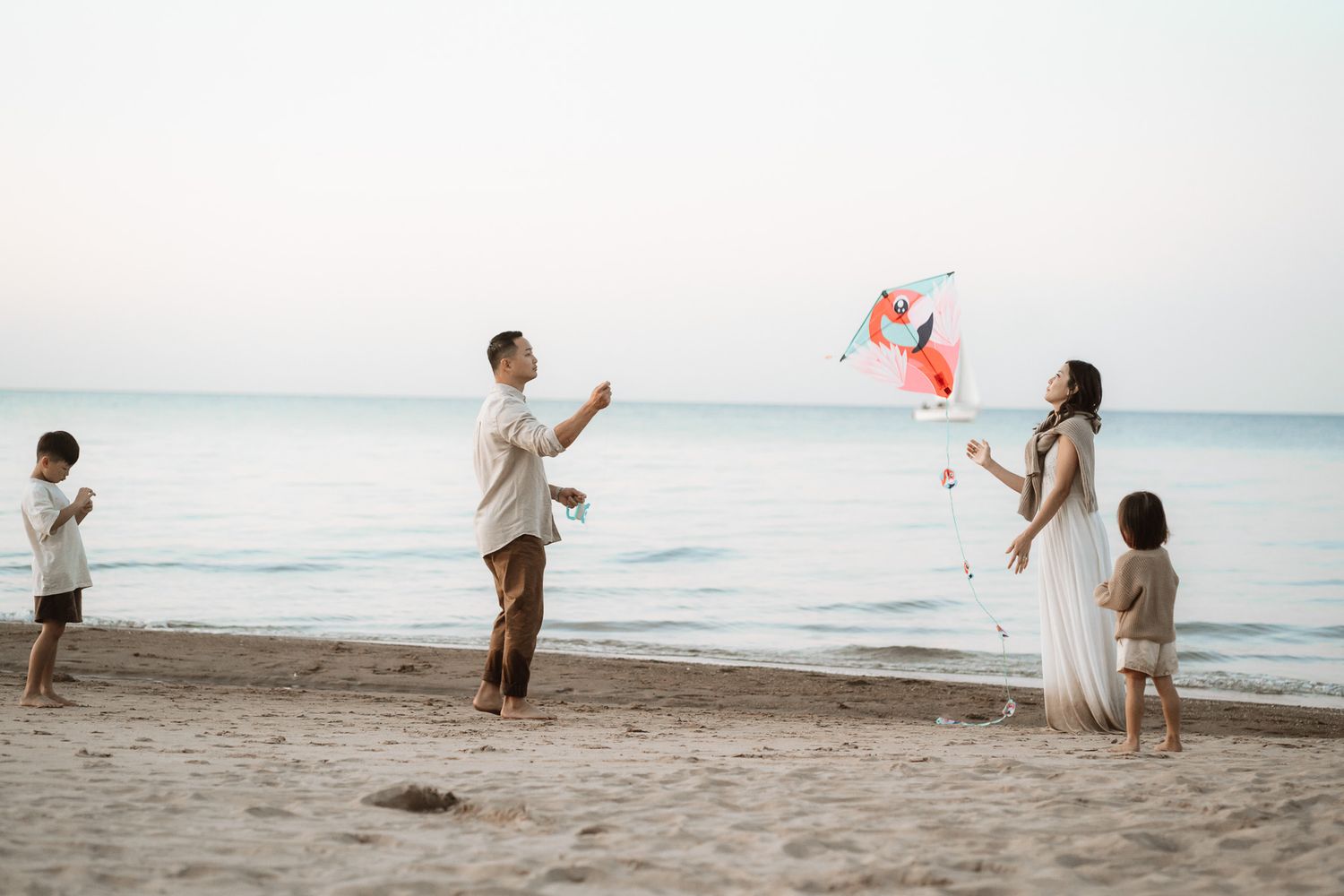 Family flying a colorful kite on a sandy beach at dusk, with calm ocean waves in the background.