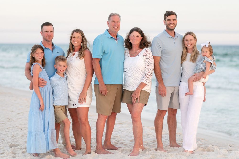 Large family posing together on a sandy beach at sunset, wearing coordinated blue and white outfits.
