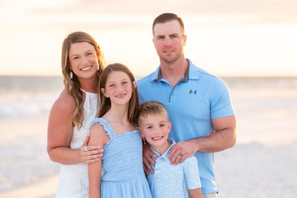 Happy family of four posing together on a beach at golden hour sunset.