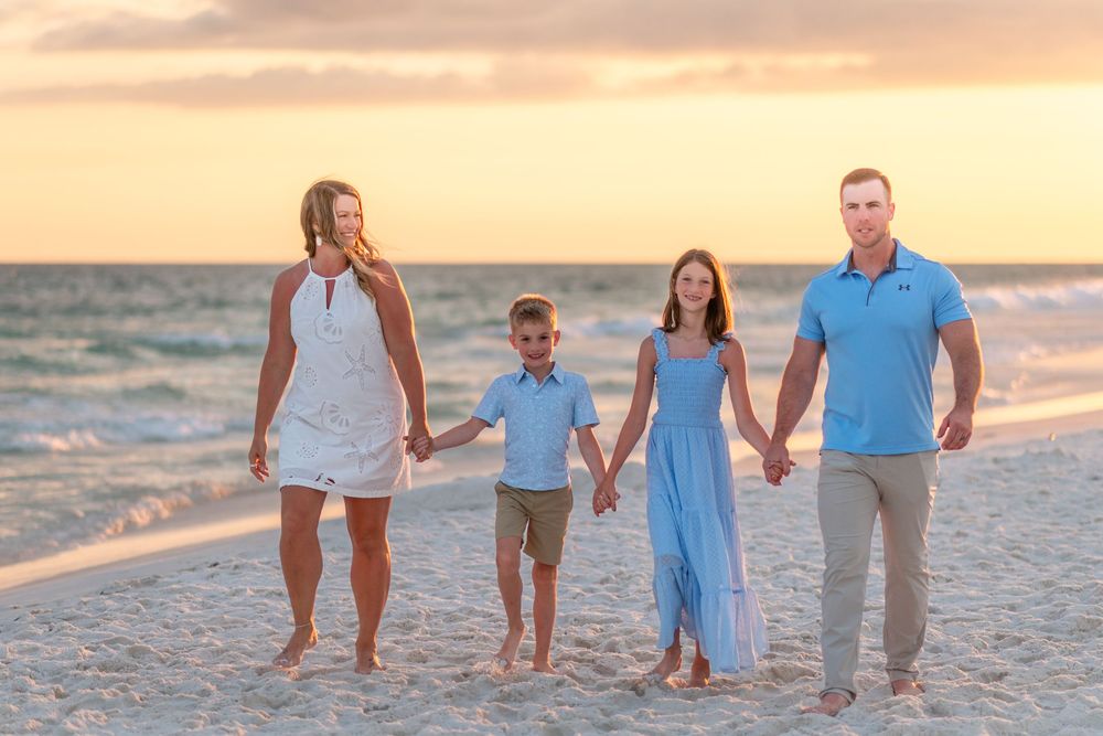 Family of four holding hands walking on a beach at sunset.