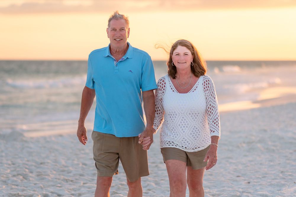 Couple holding hands and walking along a sandy beach at sunset.