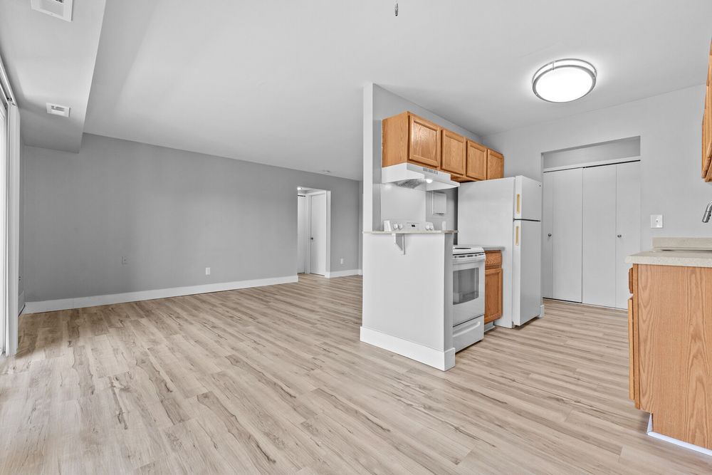 Open-concept kitchen and living area with light wood floors, white appliances, oak cabinets, and vaulted ceilings.
