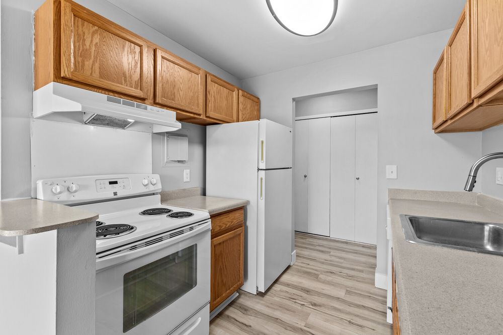 Modern kitchen with white appliances, oak cabinets, and light wood-look flooring in a bright apartment.