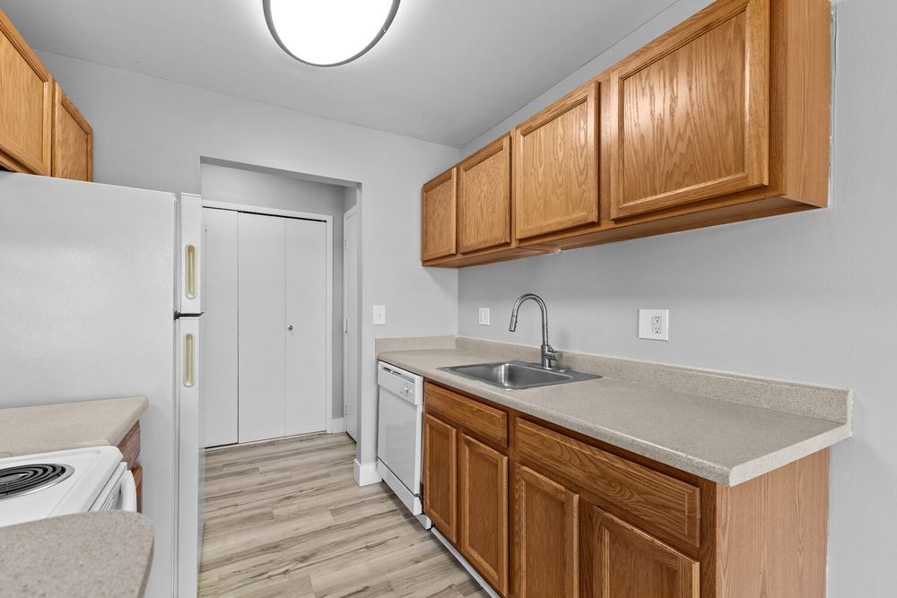 Apartment kitchen featuring oak cabinets, double sink, white dishwasher, and light hardwood-style floors.