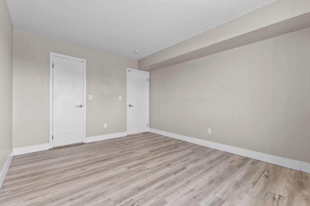 Empty bedroom with light gray walls, white doors, and light wood laminate flooring in a modern home.