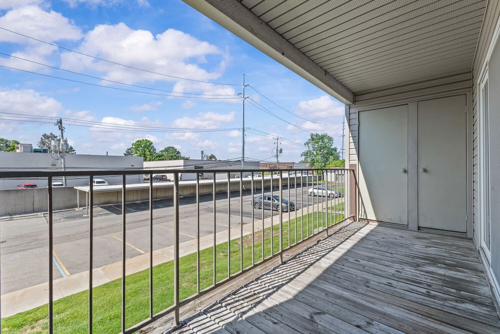 Spacious balcony with wood deck flooring, metal railing, and open views of parking lot and street.