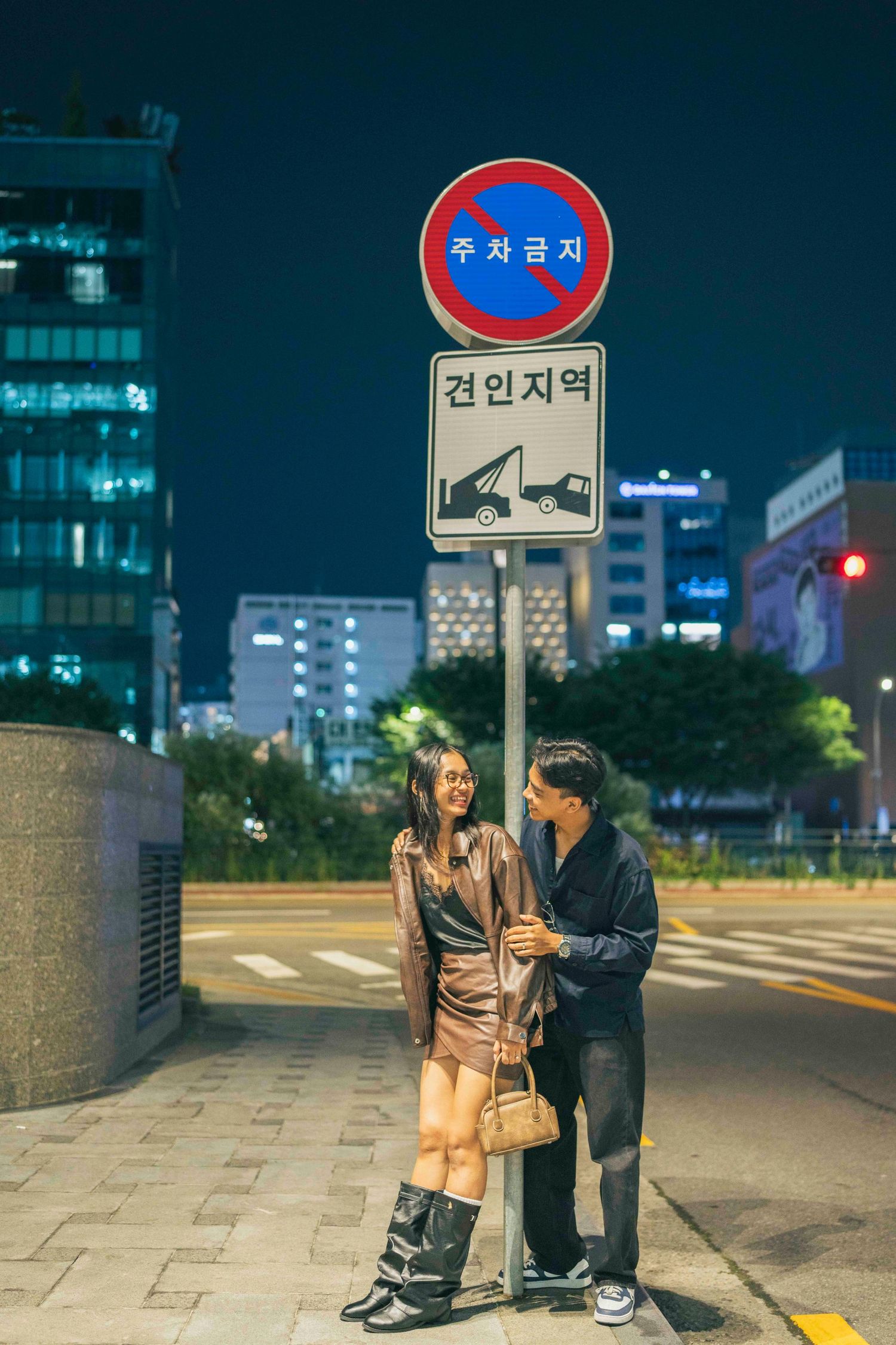 Couple standing together at night beside a Korean no-parking sign on a city street in Seoul, South Korea.
