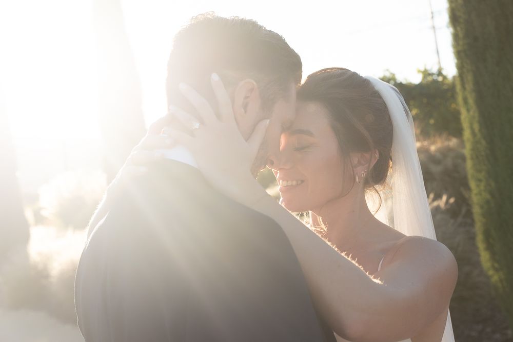 A bride and groom share a tender embrace bathed in golden sunlight during their outdoor wedding ceremony.