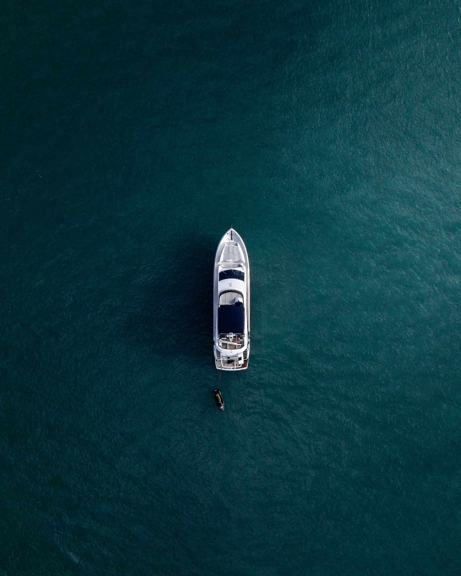 Aerial drone view of a white luxury yacht floating alone on calm deep teal ocean waters.