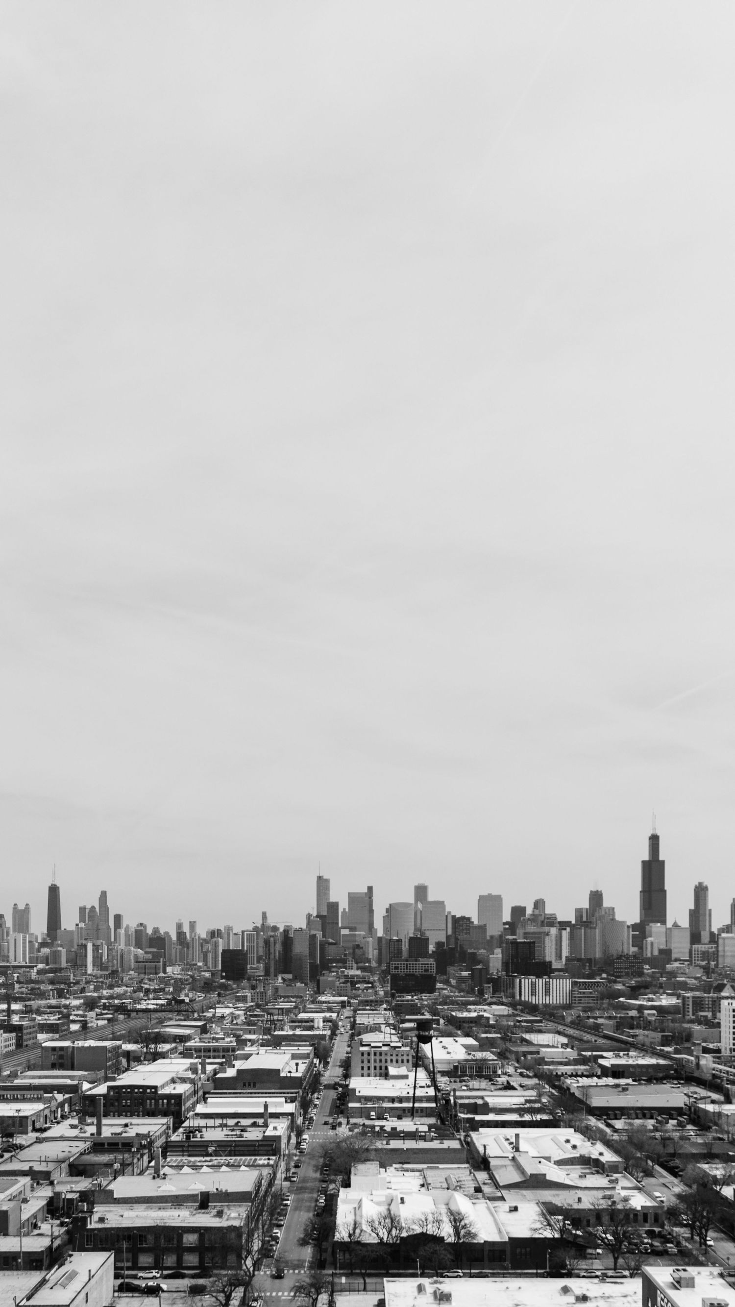 Black and white aerial view of Chicago skyline with dense urban neighborhoods and Willis Tower visible on overcast day.