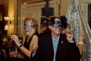 Two guests wearing decorative masquerade masks dance joyfully at a festive gala event.
