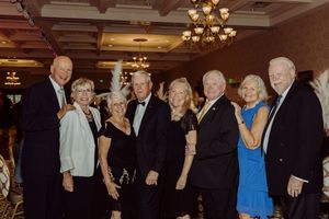Group of eight formally dressed guests pose together smiling at an elegant gala celebration.
