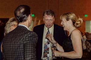 Three formally dressed guests share a lively conversation at an evening gala event.