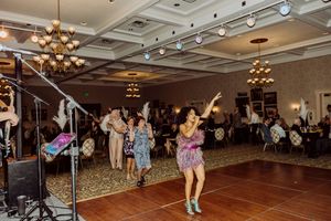 Lively performer in floral dress dancing on a ballroom floor at an elegant formal event with guests in background.